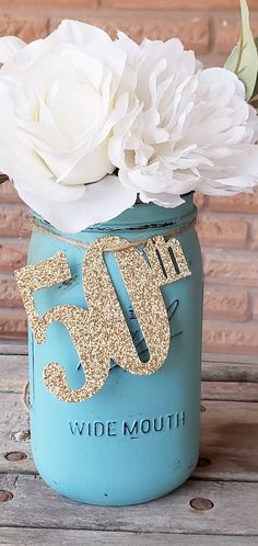 a blue mason jar with white flowers and the number fifty five in gold glitter on it