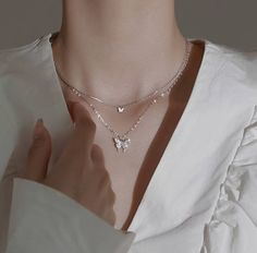 a woman wearing a white shirt with a silver necklace on her neck and hands in front of her chest