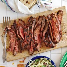 sliced steak on cutting board with salad and utensils next to plated food