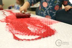 a woman is using a red paint brush to create a heart on a white table