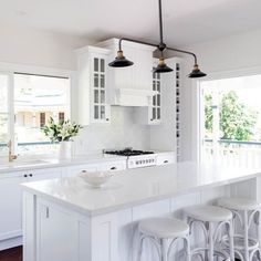 a kitchen with white cabinets and stools next to an island in front of a window