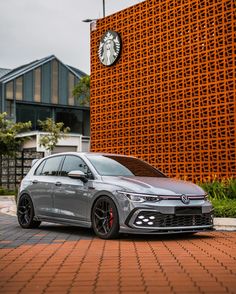 a silver car parked in front of a building with a clock on it's side