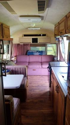 the inside of a camper with pink couches and wood cabinets in front of it