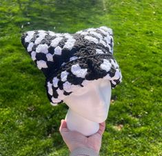 a hand holding up a black and white knitted hat on top of a head