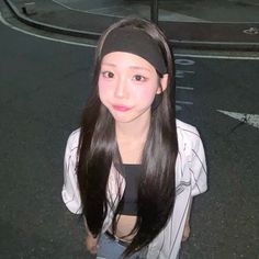 a girl with long black hair standing in the street