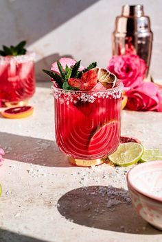 two glasses filled with red liquid and garnished with limes, surrounded by pink flowers