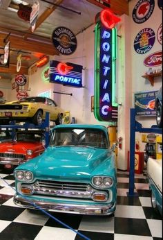 several classic cars parked in a garage with neon signs on the wall and checkered floor