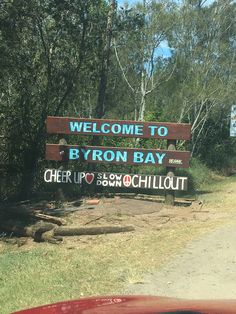 a welcome sign to byron bay on the side of a road with trees in the background