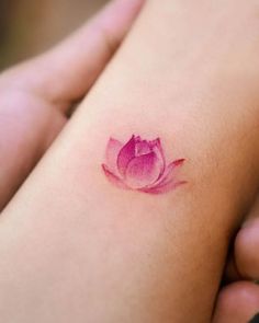 a small pink flower tattoo on the back of a woman's left arm,