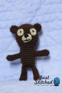 a crocheted brown teddy bear with big eyes standing upright on a white blanket