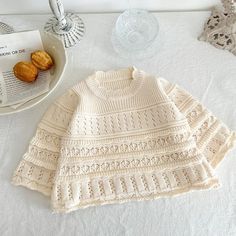 a white knitted sweater next to a bowl of crochet and some pastries