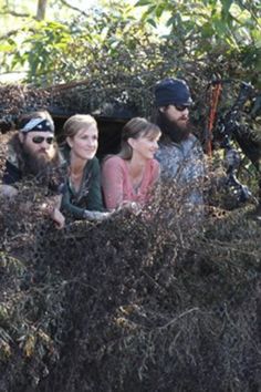 three people are sitting in the bushes looking at something