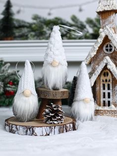 three small white gnomes sitting on top of a tree stump in front of a house