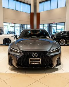 the front end of a gray sports car in a showroom with two other cars