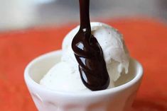 a scoop of ice cream with chocolate sauce on top in a small white cup sitting on an orange table