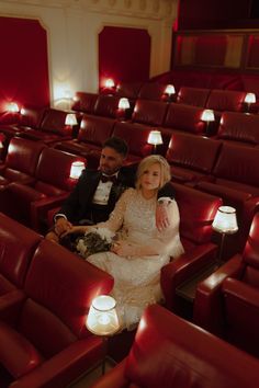 a man and woman are sitting in the middle of an empty theater with red seats