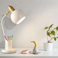 a desk lamp sitting on top of a white table next to a potted plant