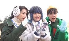 three young men standing next to each other in front of the ocean wearing winter clothing