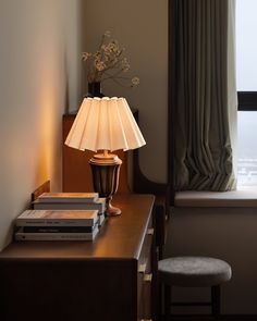 a lamp sitting on top of a wooden table next to a window with drapes