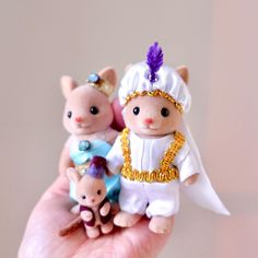 a hand holding two tiny figurines that look like cats and kittens in costumes