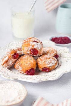 powdered sugar covered pastries on a white plate with raspberries in the foreground