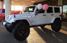 a white jeep parked in front of a building with balloons on the top of it