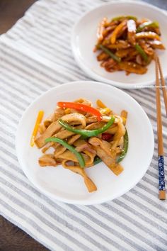 two white plates topped with stir fry and veggies next to chopsticks