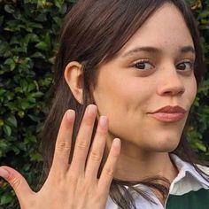 a woman holding her hand up to her face while wearing a white shirt and green vest