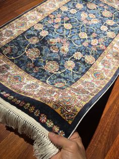 a person is holding up a rug on the floor in front of a wooden table