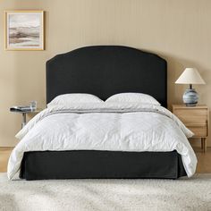 a bed with a black headboard and white comforter in a beige room next to a night stand