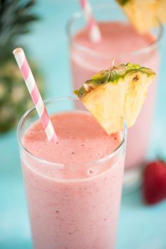 two glasses filled with pink smoothie and topped with a pineapple on the side