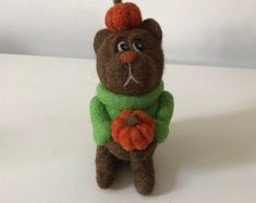 a brown teddy bear wearing a green sweater and holding an orange pumpkin on its head