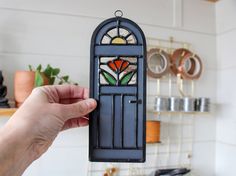 a hand is holding up a stained glass door in front of a shelf with pots and pans on it