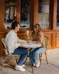 a man and woman sitting at a table with drinks in front of a storefront