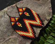 a pair of beaded earrings sitting on top of a rock next to a plant