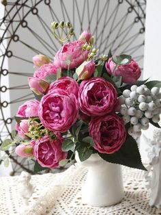 a white vase filled with pink flowers on top of a table