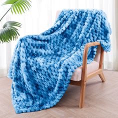 a blue blanket sitting on top of a wooden chair next to a potted plant