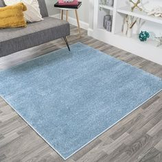 a blue rug in a living room next to a gray couch and bookcases