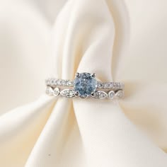 a blue diamond ring sitting on top of a white satin cloth with diamonds around it