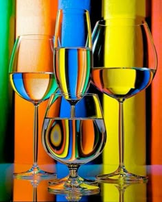 three wine glasses sitting next to each other in front of colorful wallpaper with multicolored bars behind them