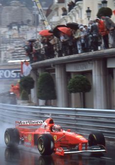 a man driving a red race car down a wet street in front of a crowd