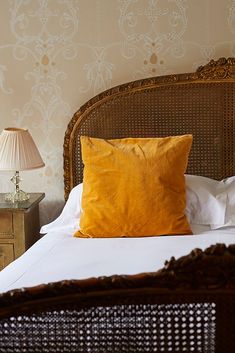 a bed with white sheets and yellow pillows on it, next to a night stand