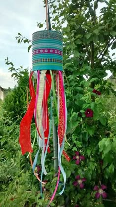 a wind chime hanging from a tree in the middle of some bushes and flowers