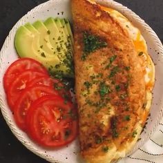 a white plate topped with an omelet next to sliced tomatoes and cucumbers