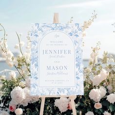 a welcome sign sitting on top of a wooden easel next to flowers and water