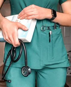 a woman in green scrubs holding a medicine box and a stethoscope