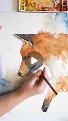 someone is painting a fox with watercolors on the paper and holding a paintbrush