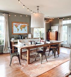 a dining room table with chairs and lights hanging from it's ceiling in front of two windows