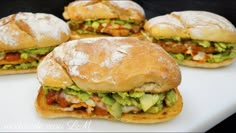 four sandwiches with meat, lettuce and tomato on them sitting on a white plate