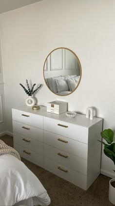 a bedroom with white furniture and a round mirror on the wall above it's dresser